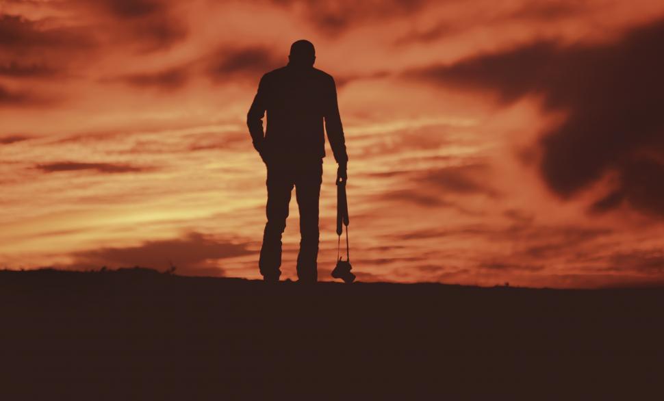 Free Image of Man holding camera with red sunset sky as background 