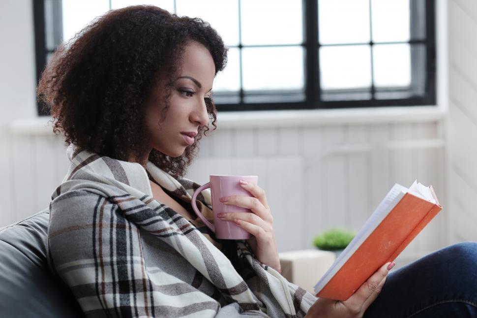 Free Image of Woman reading a book while drinking a hot beverage 