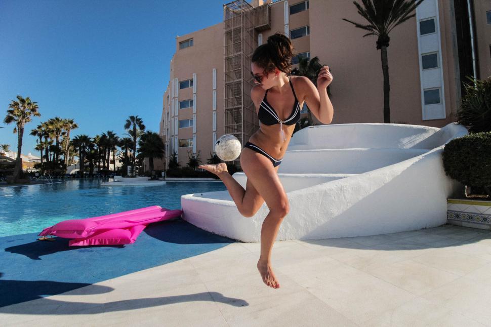 Free Image of Woman beside pool kicking football 