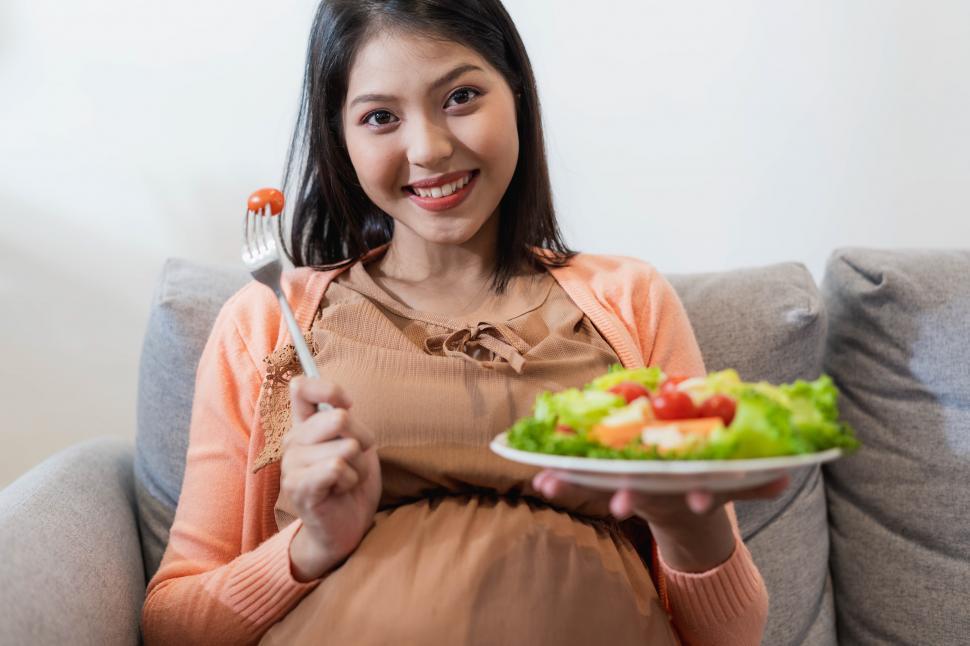 Free Image of Happy pregnant Asian woman sitting and eating natural food 