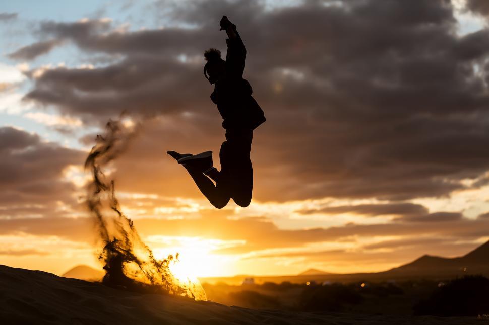 Free Image of Unrecognizable person jumping on sandy shore during sunset 