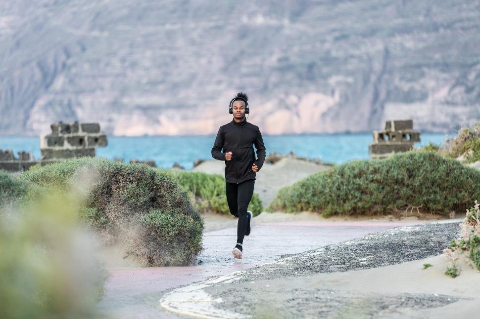 Free Image of Black athlete in headphones running on seashore 