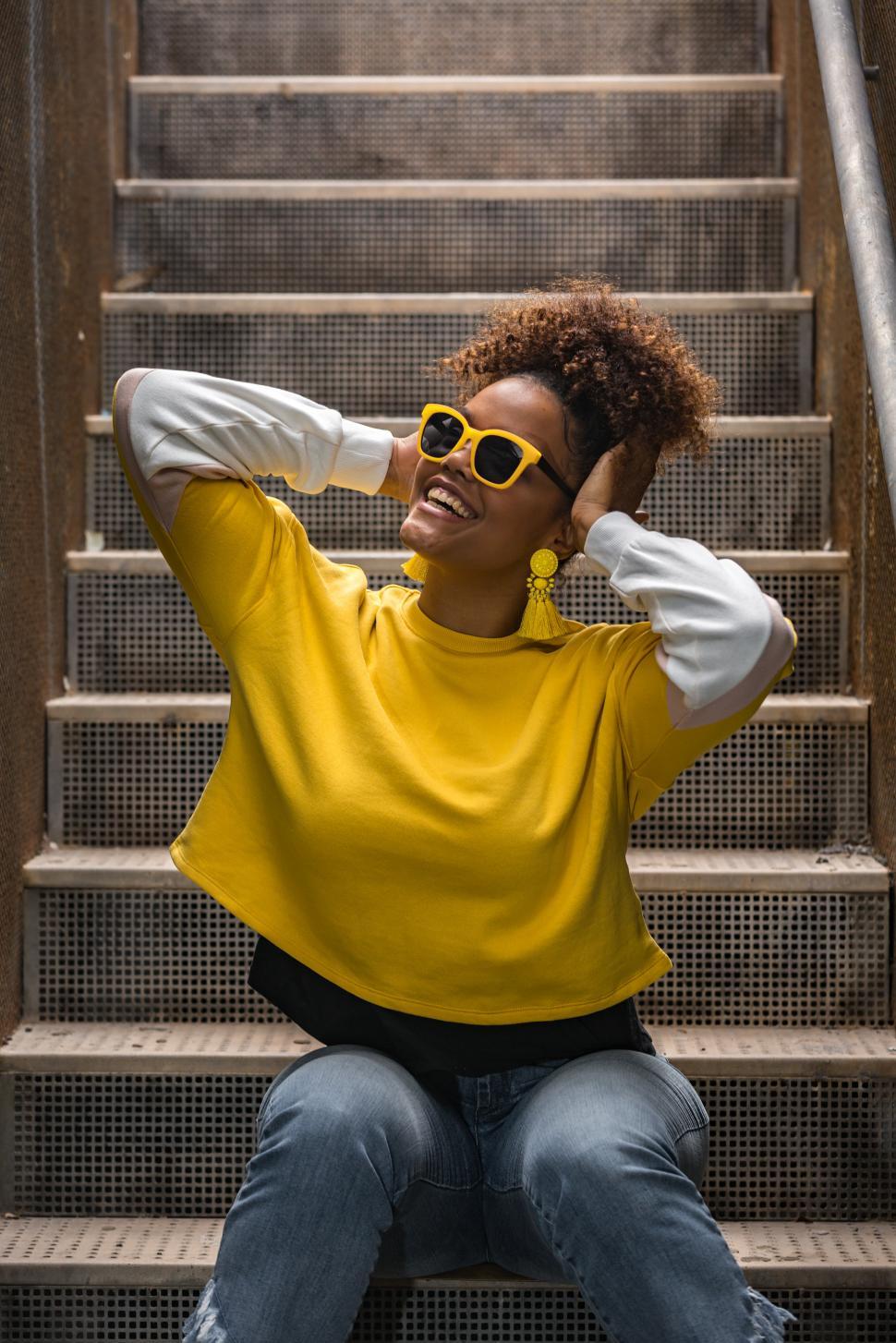 Free Image of Happy black hipster woman in trendy wear and sunglasses sitting 