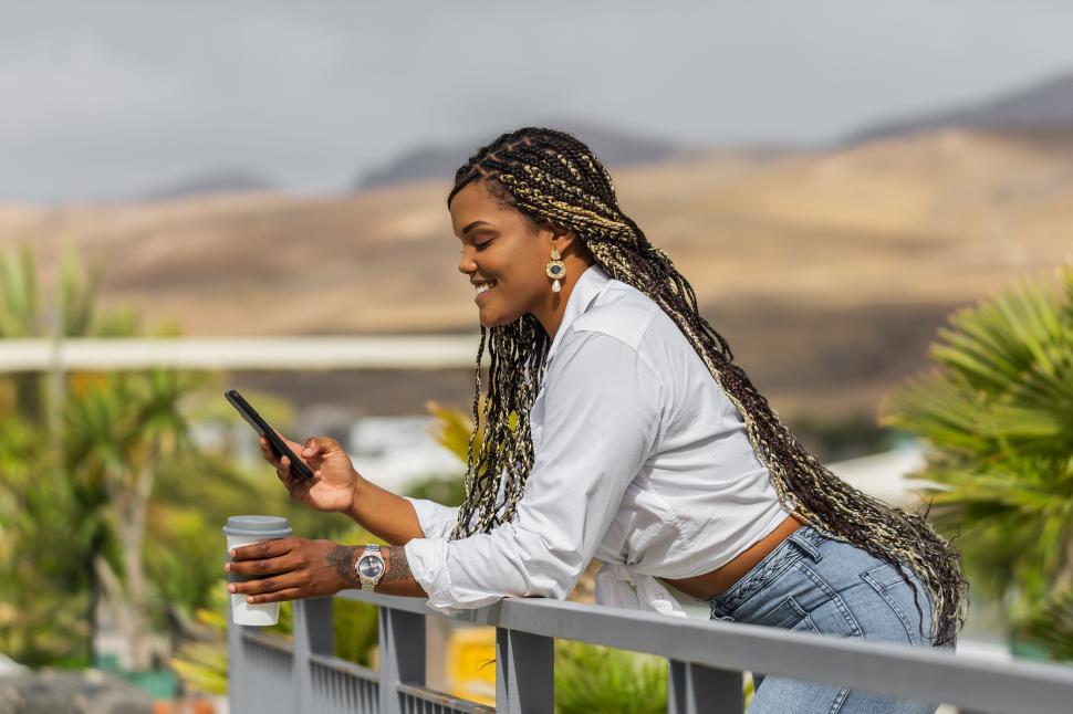 Free Image of Woman using phone leaning on handrail outdoors 