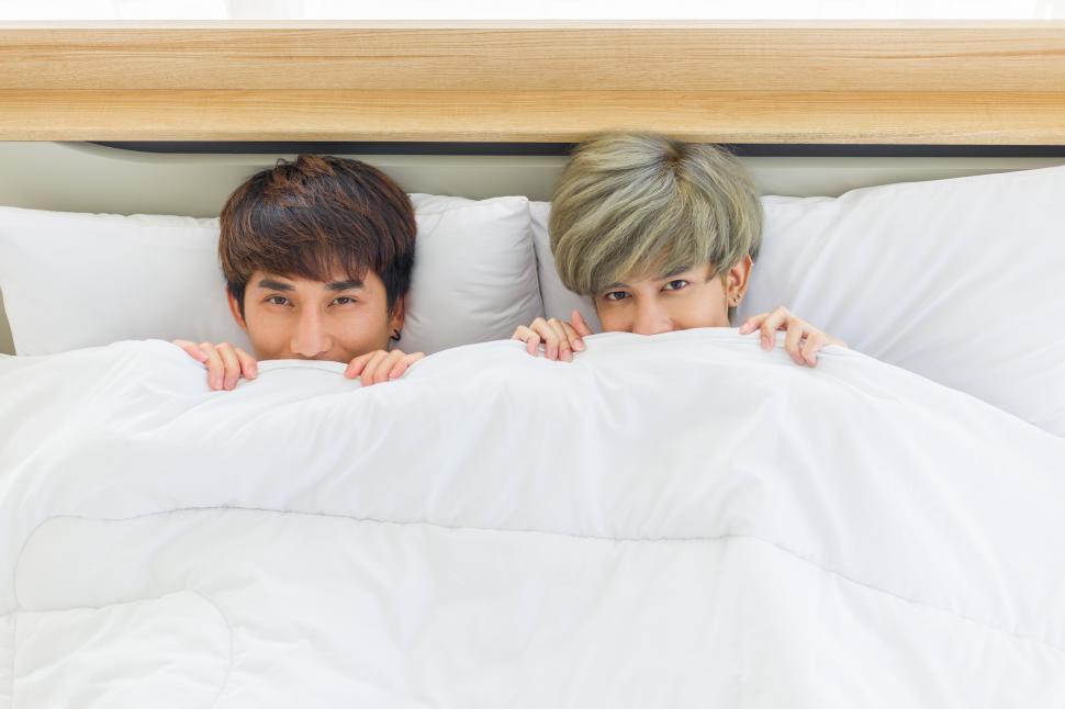 Men peeking out from under white bedsheets