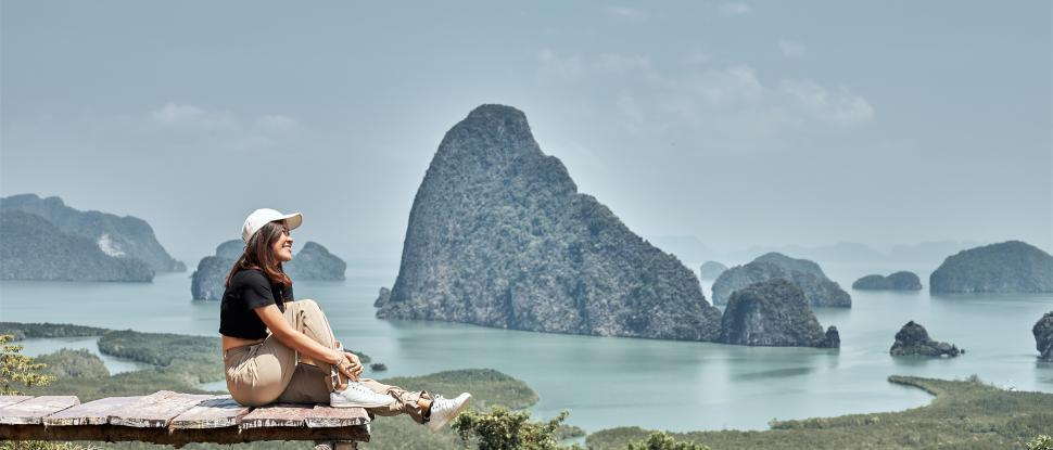Free Image of Young woman sits on a wooden bridge with a beautiful sea backdrop 