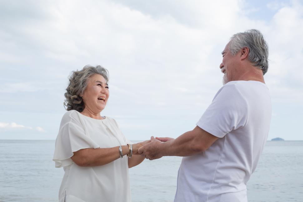 Free Image of Senior couple holding hands together and dancing at the beach 