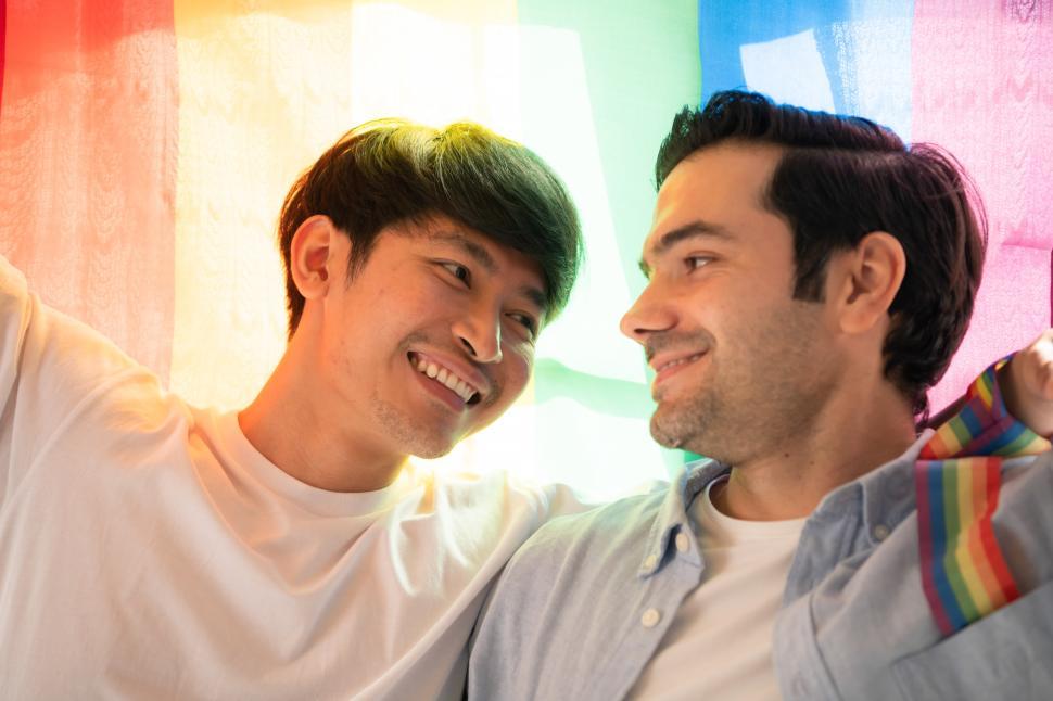 Two men share a smile, lit by colors of the pride flag