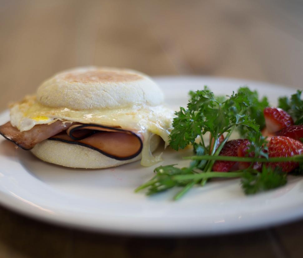 Free Image of A sandwich with ham and cheese and a side of parsley on a white plate 