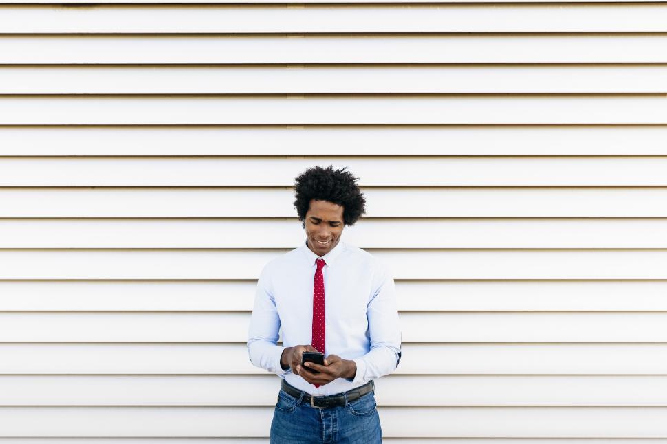 Free Image of Black Businessman using a smartphone with a white blinds background 
