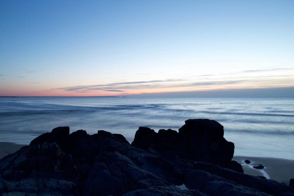 Free Image of A rocky beach with a body of water and a sunset 
