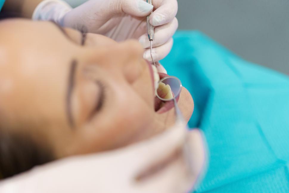 Free Image of Dentist checking the inside of her patient s teeth with a dental mirror. 