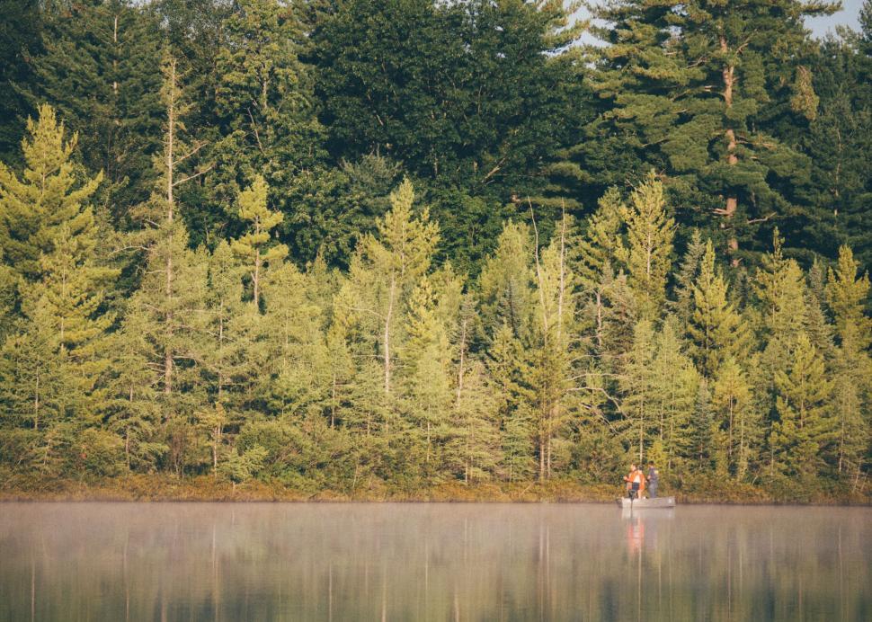 Free Image of A group of people on a boat in a lake surrounded by trees 