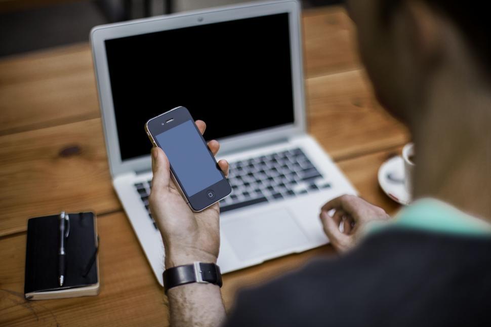 Free Image of A person holding a phone in front of a laptop 