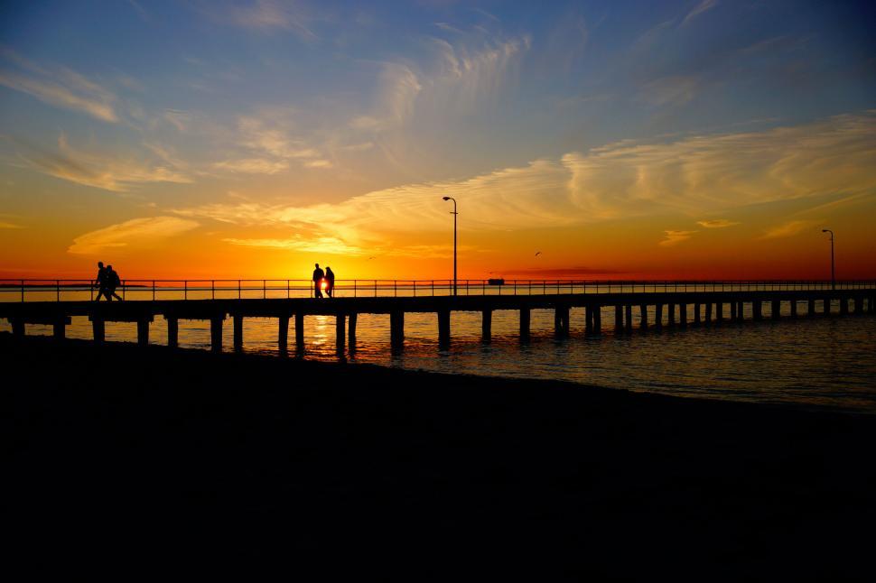 Free Image of A couple of people walking on a bridge over water 