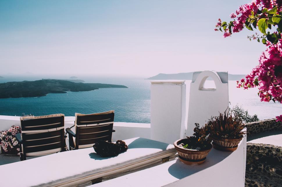 Free Image of Chairs and chairs on a white wall overlooking a body of water 