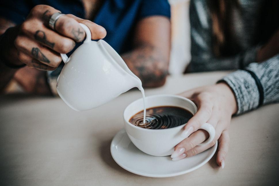 Free Image of A person pouring milk into a cup of coffee 