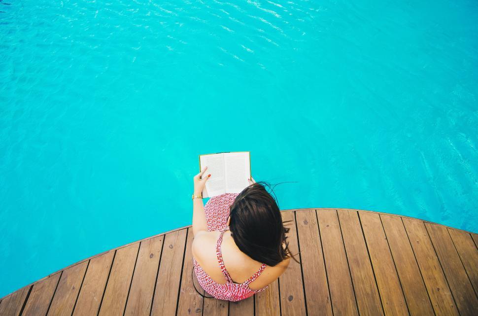Free Stock Photo of A woman sitting on a deck by a pool reading a