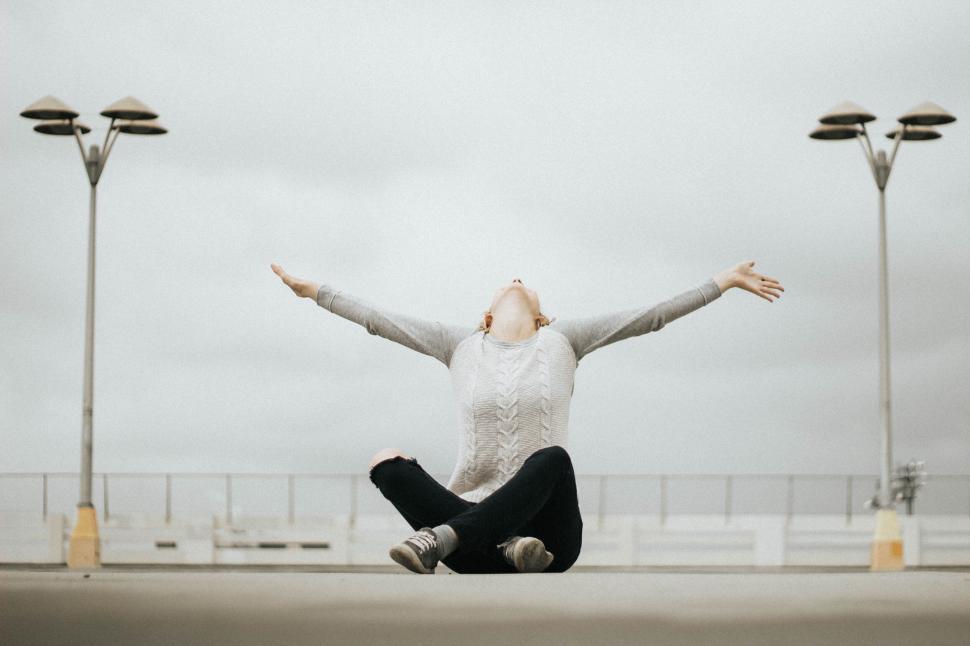 Free Image of A woman sitting on the ground with her arms outstretched 