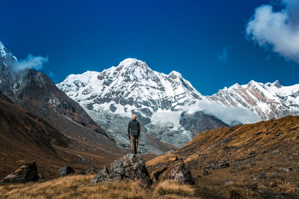 Free Image of A man standing on a rock in front of a snowy mountain 