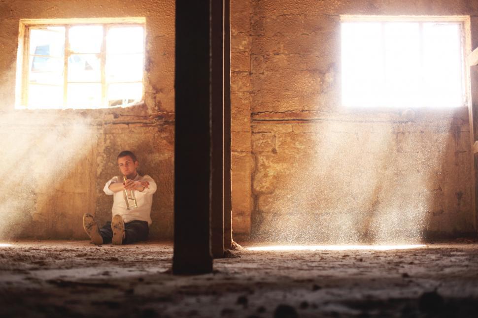 Free Image of A man sitting on the floor in a room with a bottle 