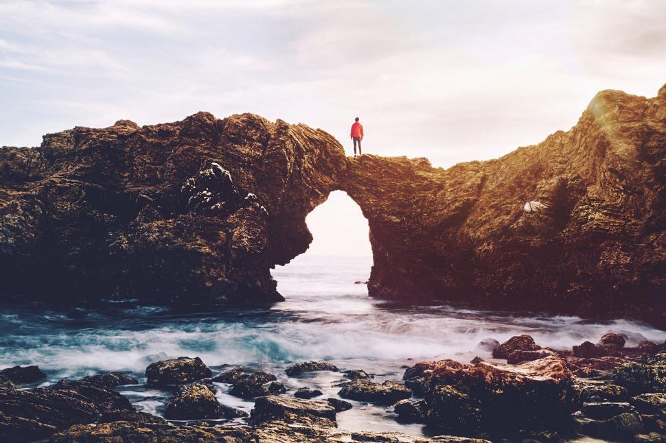 Free Image of A person standing on a rock bridge over water 