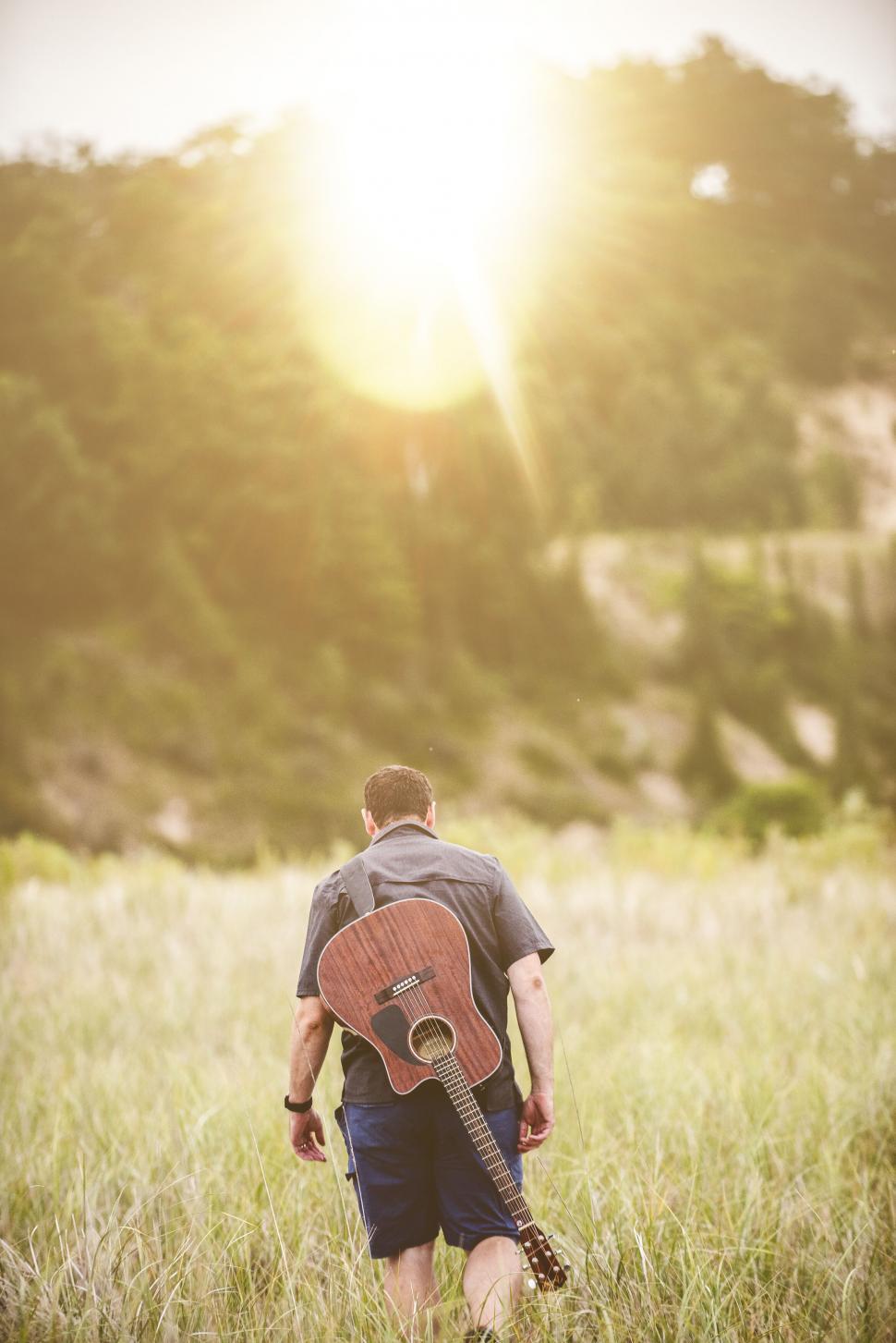 Free Image of Man with guitar walking in field 