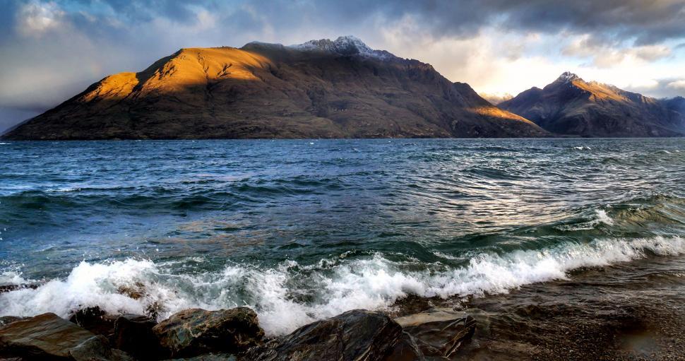 Free Image of Stormy waves crashing against mountain backdrop 