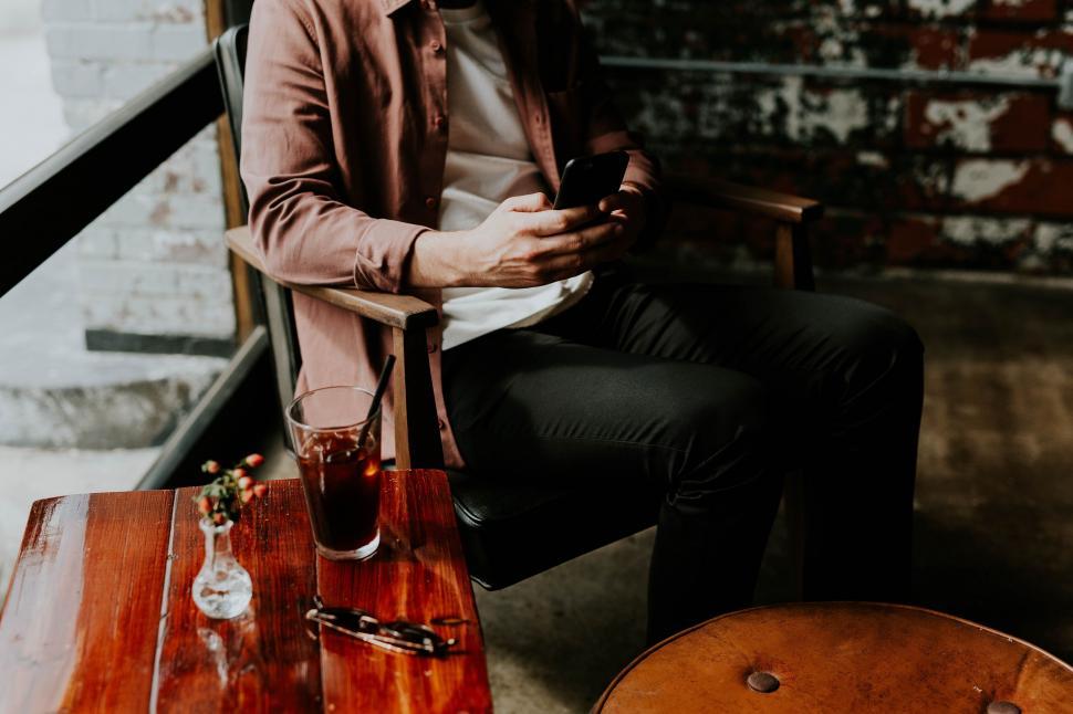 Free Image of Man at a cafe with drink texting on phone 