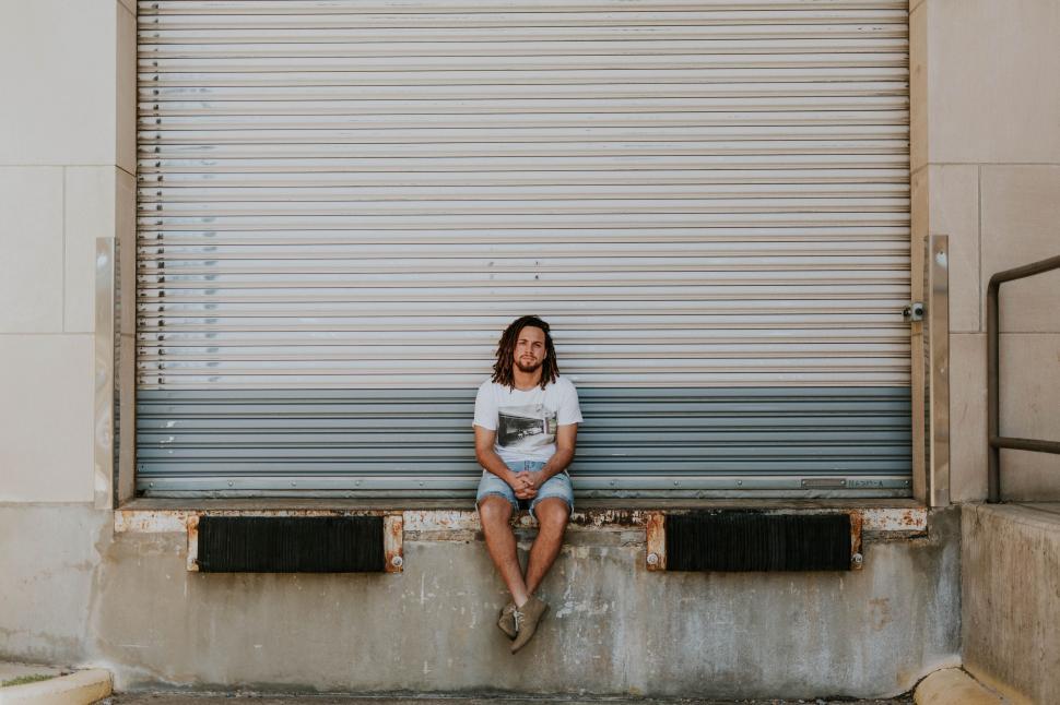 Free Image of Man sitting alone in front of a metal shutter 
