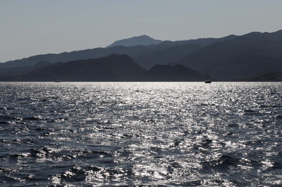 Free Image of Sparkling sea with mountain silhouette at sunset 