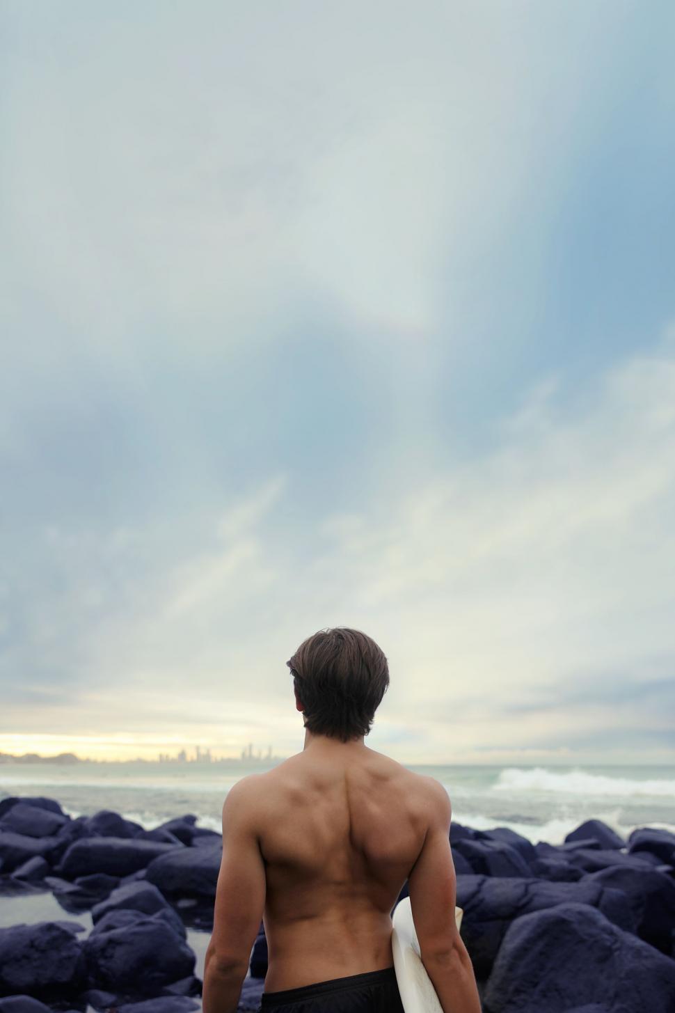 Free Image of Man looking at cityscape from rocky beach 