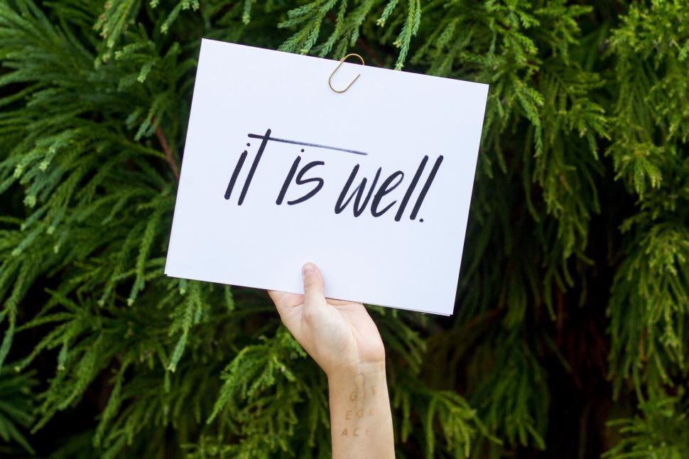 Free Image of Hand holding a sign  It is well  with foliage 