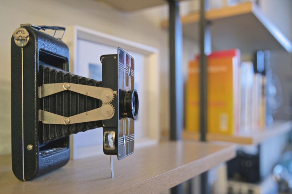 Free Image of Vintage camera on a bookshelf with books in the background 