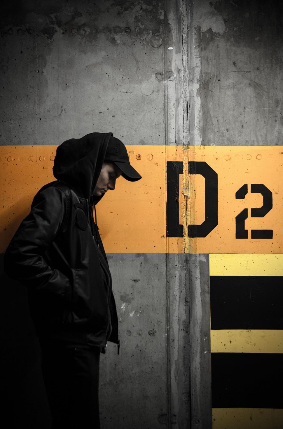 Free Image of Hooded figure by a yellow striped wall 