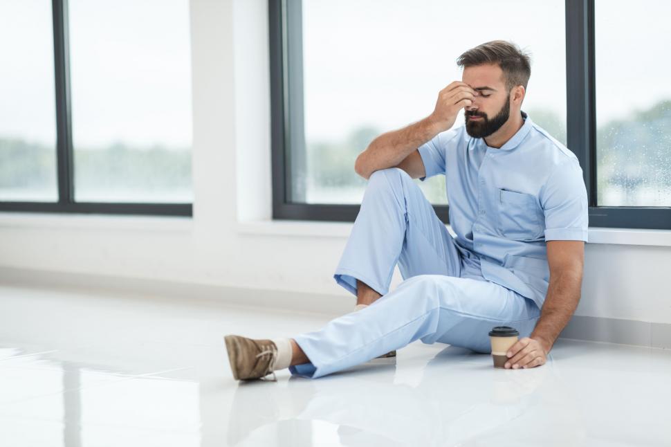 Free Image of Exhausted male nurse sitting on the floor 