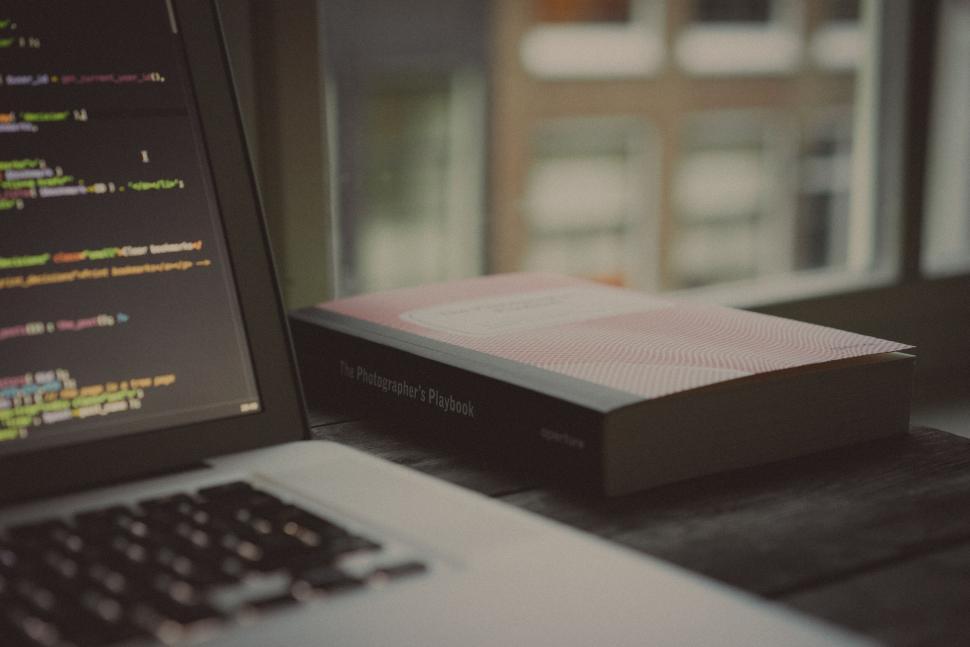 Free Image of Laptop beside book on modern coding 