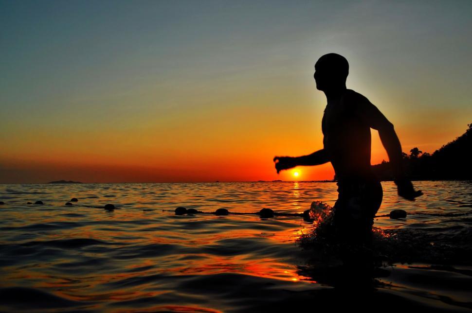 Free Image of Silhouetted person in water at sunset 