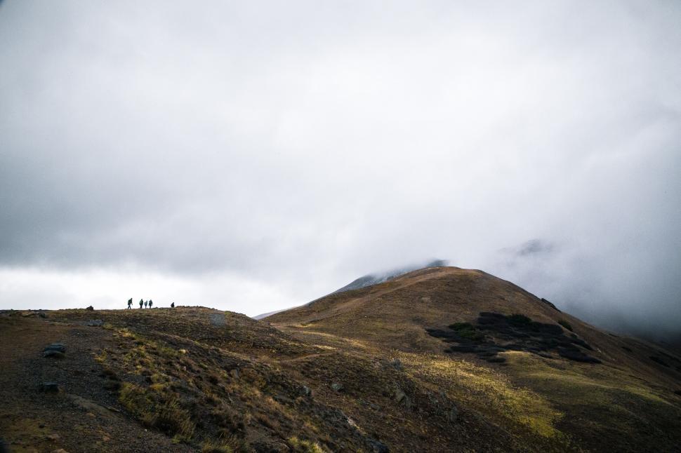 Free Image of Hikers on a mountain under cloudy skies 