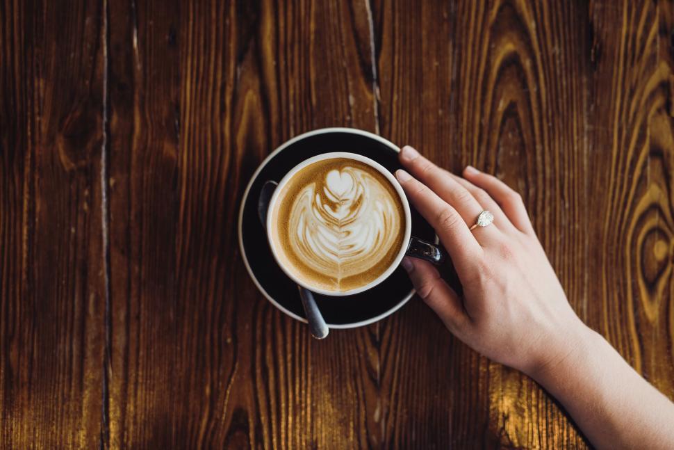 Free Image of Hand holding a cup of cappuccino with art 