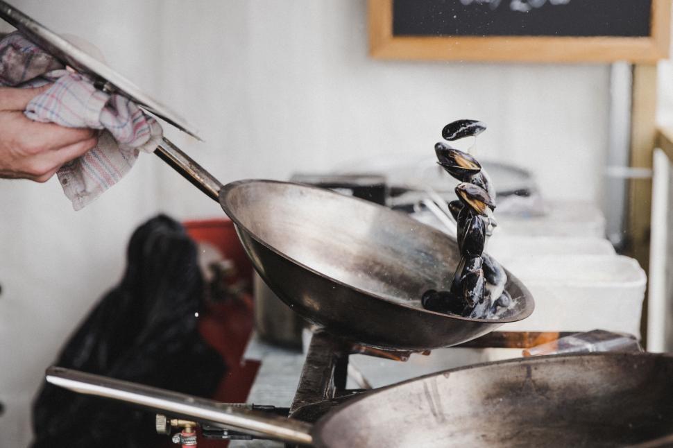 Free Image of Chef tossing mussels in a hot pan at outdoor stall 
