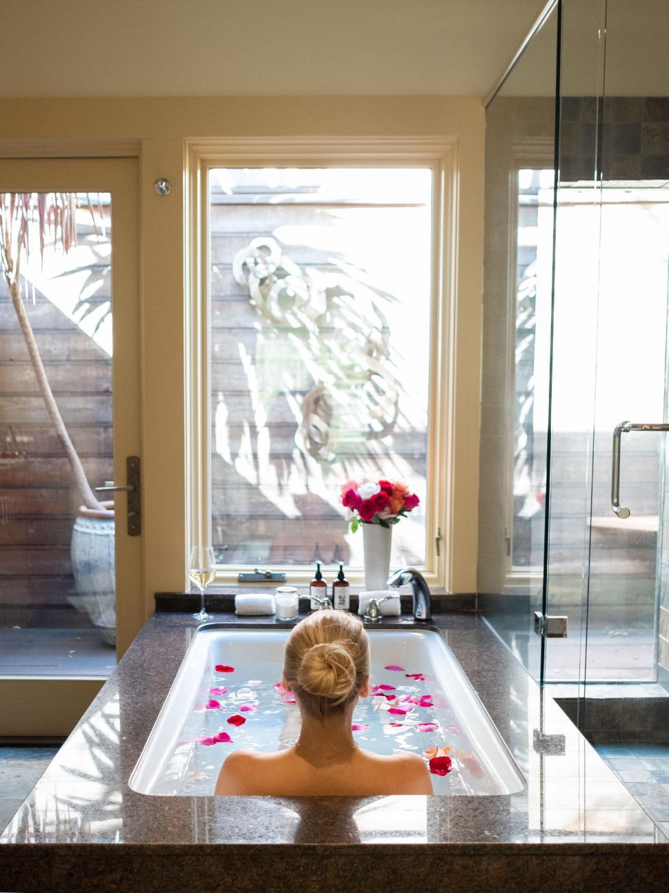 Free Image of Woman relaxing in a bath with flower petals 
