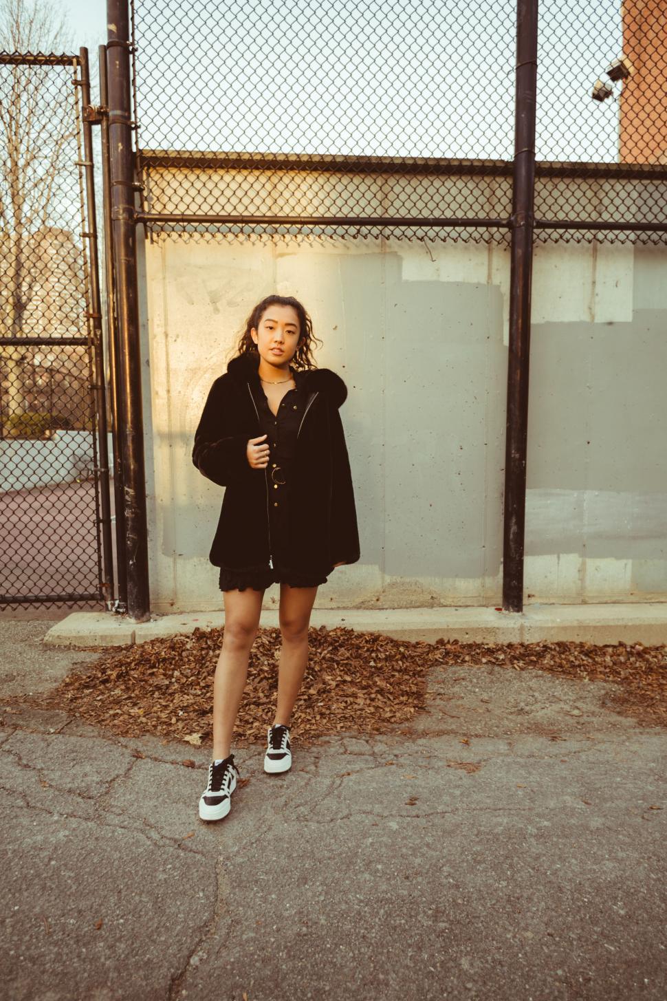 Free Image of Woman in black coat standing by fence 