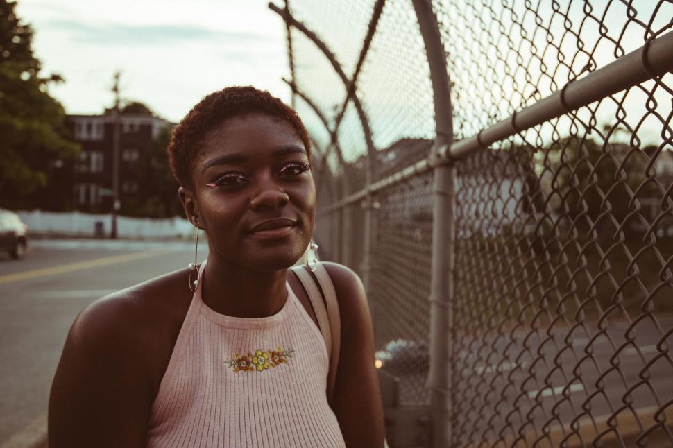 Free Image of Young woman by a chain-link fence at dusk 