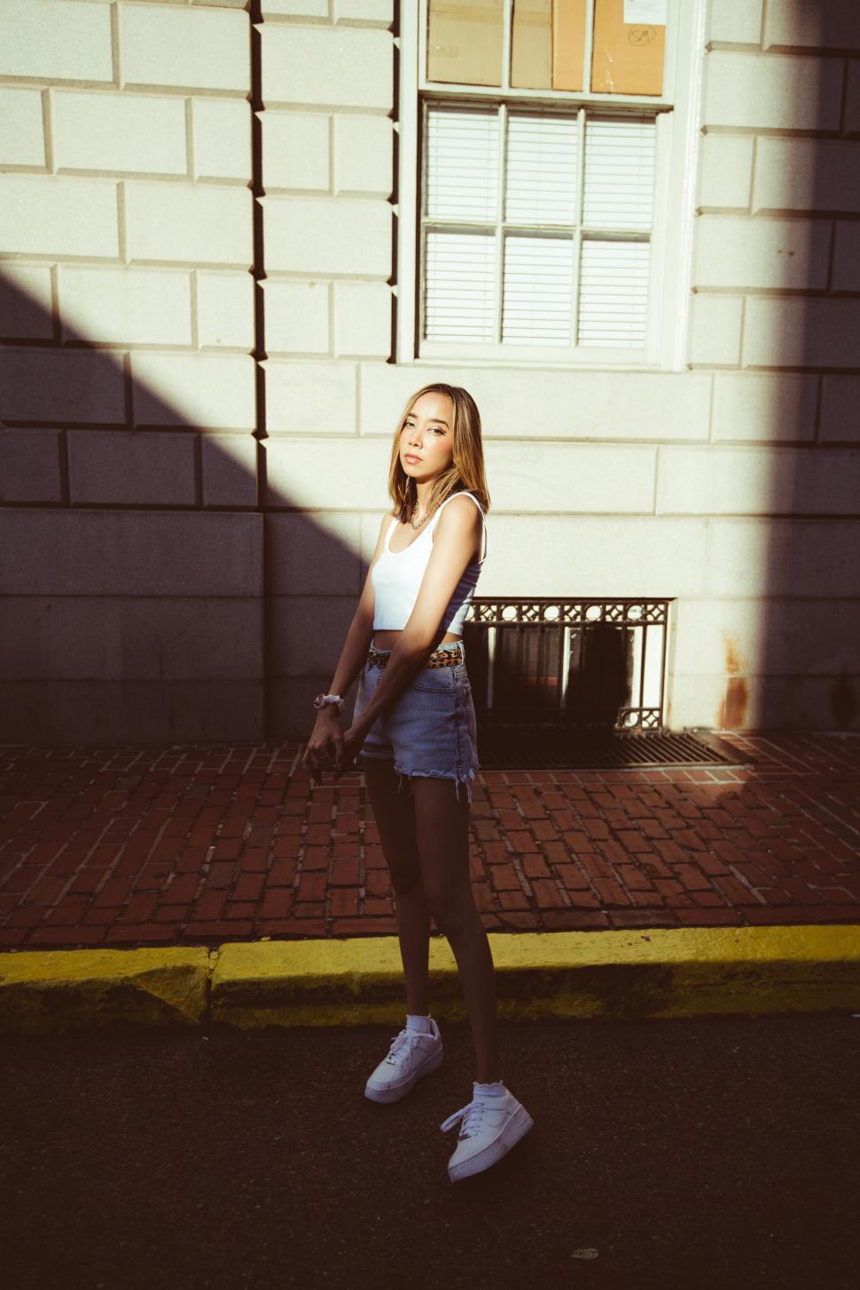 Free Image of Young woman in sunlight against urban wall 