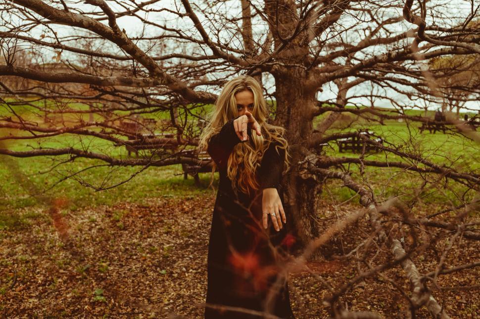 Free Image of Mysterious woman standing by leafless tree 