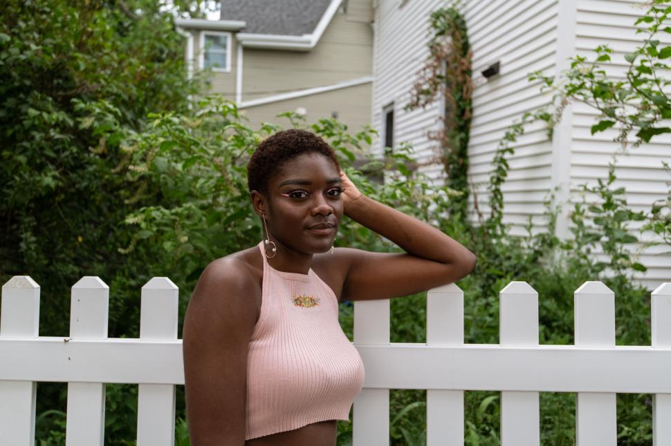 Free Image of Woman posing by a white picket fence 
