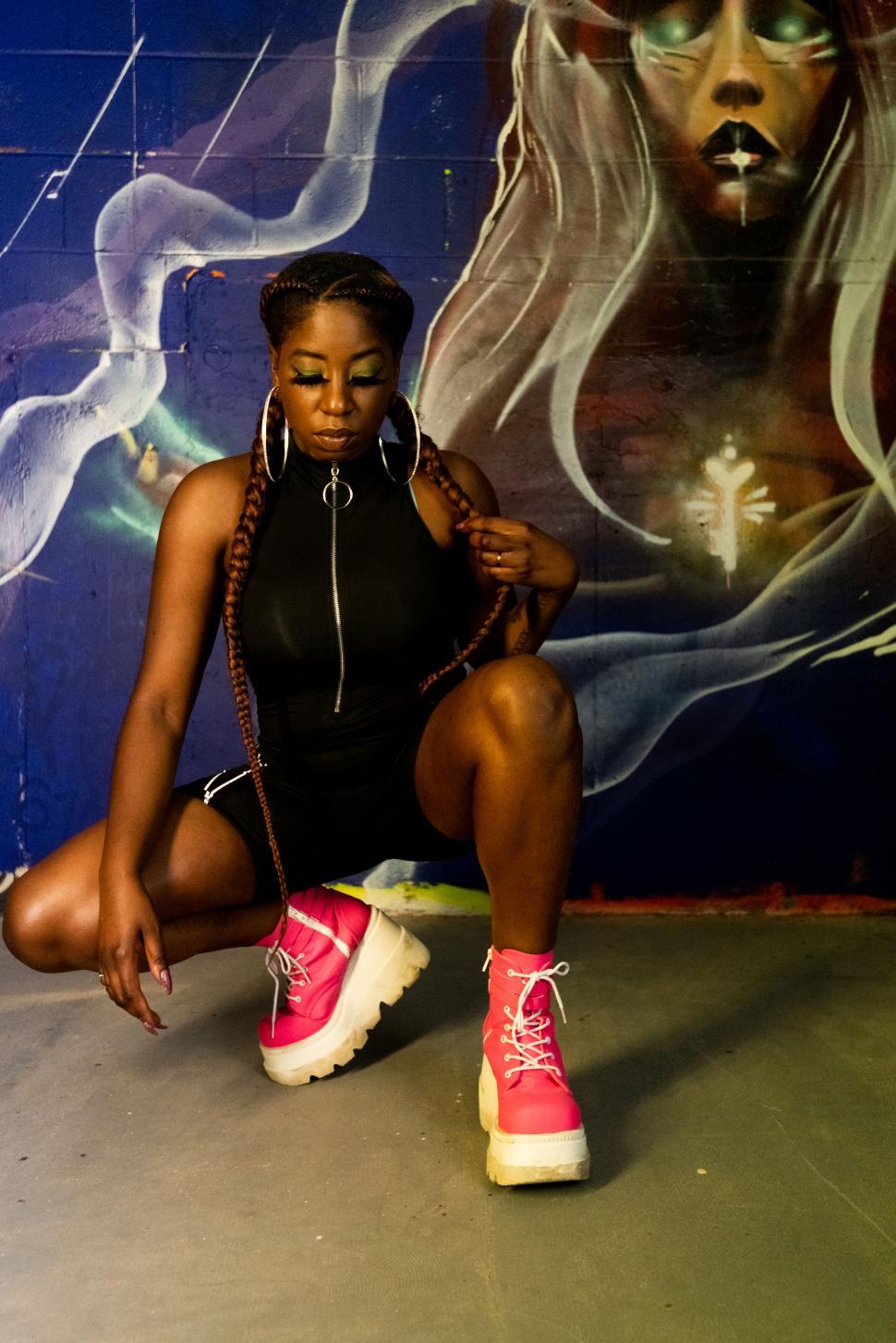 Free Image of Stylish woman squatting in front of mural 