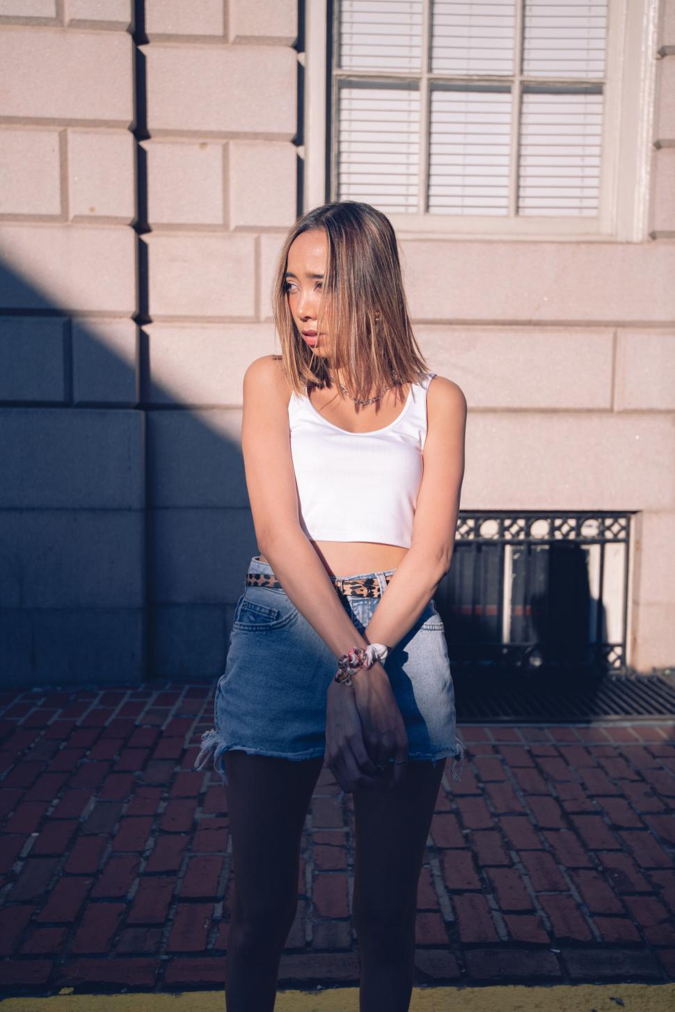 Free Image of Young woman in white top leaning on wall 