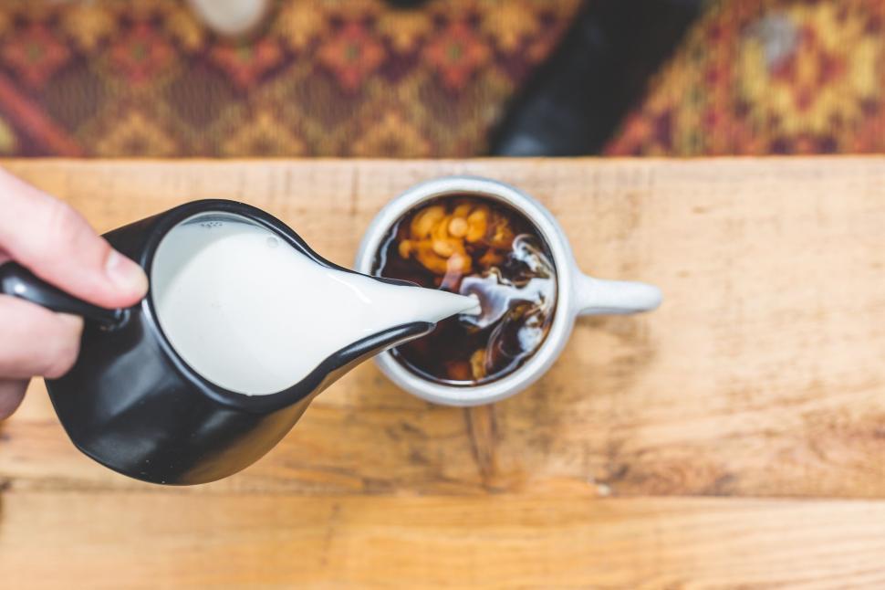 Free Image of Pouring milk into coffee at a table 